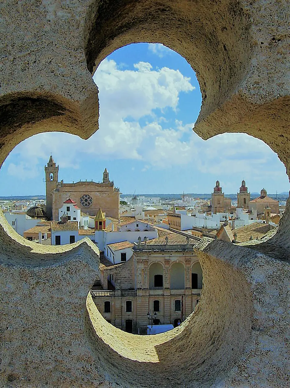 Vista d’una ciutat i la seva catedral a través d’una finestra de pedra en forma de trèvol
