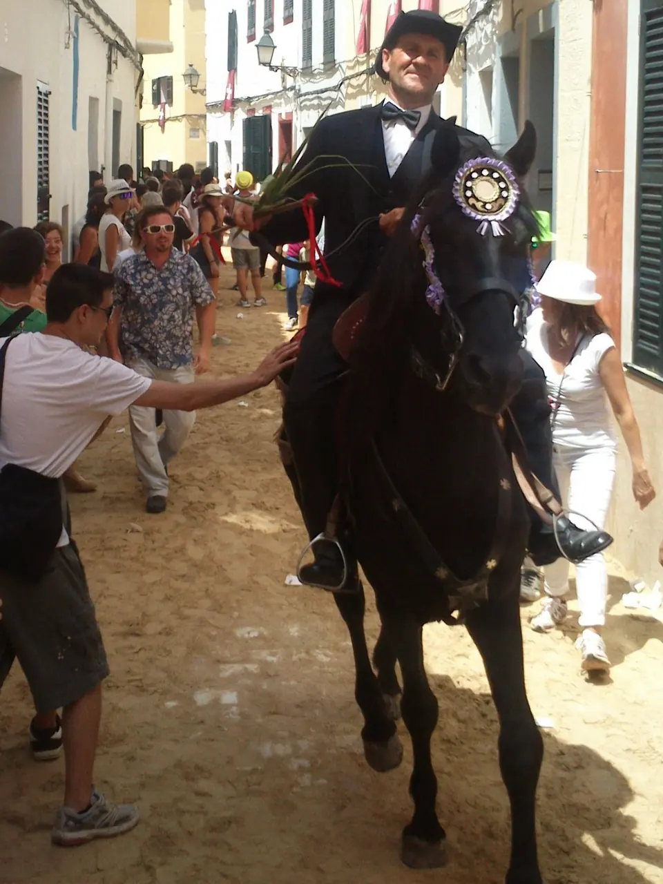 Genet amb levita sobre un cavall en un carrer estret entre la gent