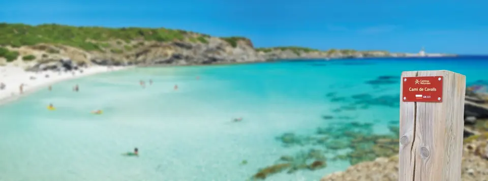 Platja d’aigües turquesa amb un pal informatiu vermell