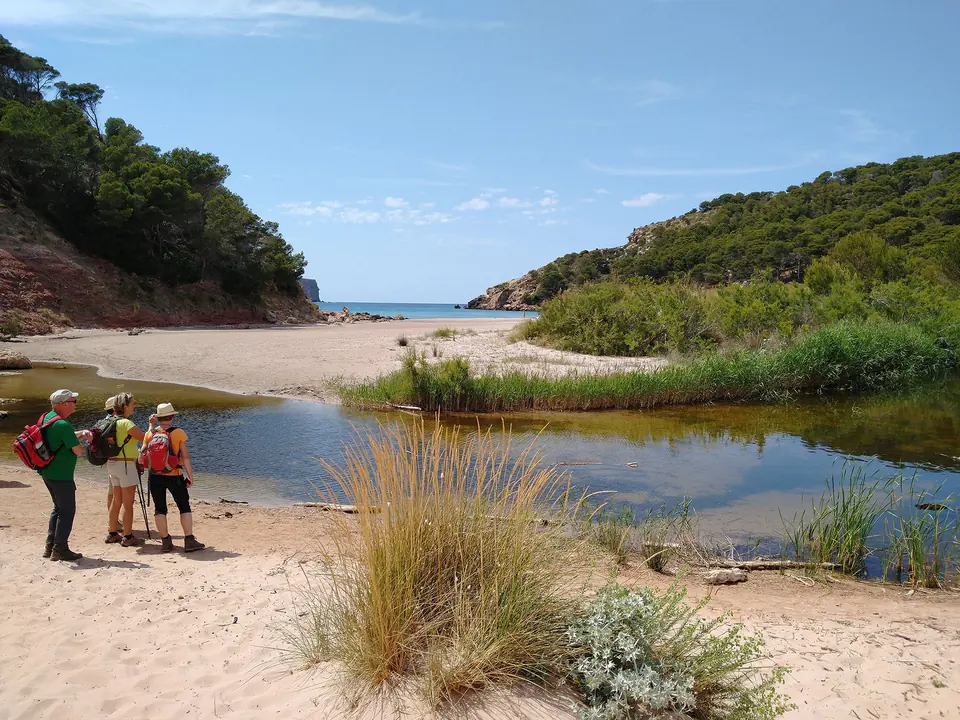 Excursionistes en una platja de sorra vora la desembocadura d’un barranc