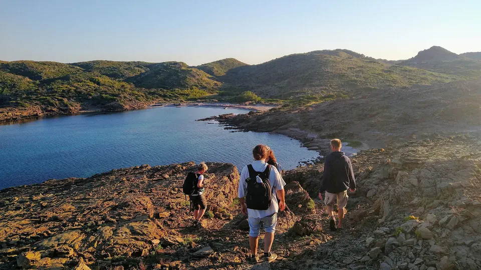 Excursionistes davallant per roques amb una badia al fons