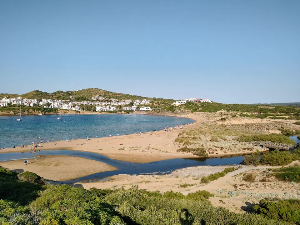 Cala Tirant: platja amb una desembocadura i un poble al fons