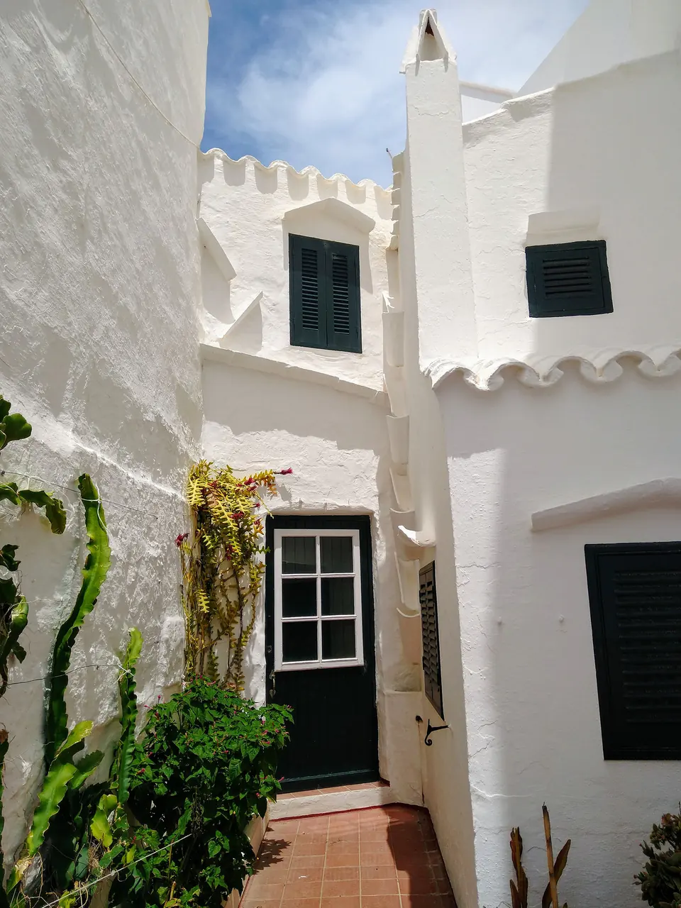 Façana blanca emblanquinada amb finestres verdes i plantes