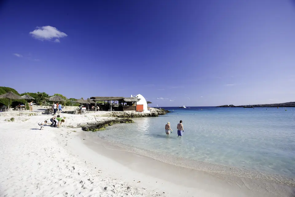Binibèquer: platja de sorra blanca amb aigües cristal·lines i un petit xiringuito