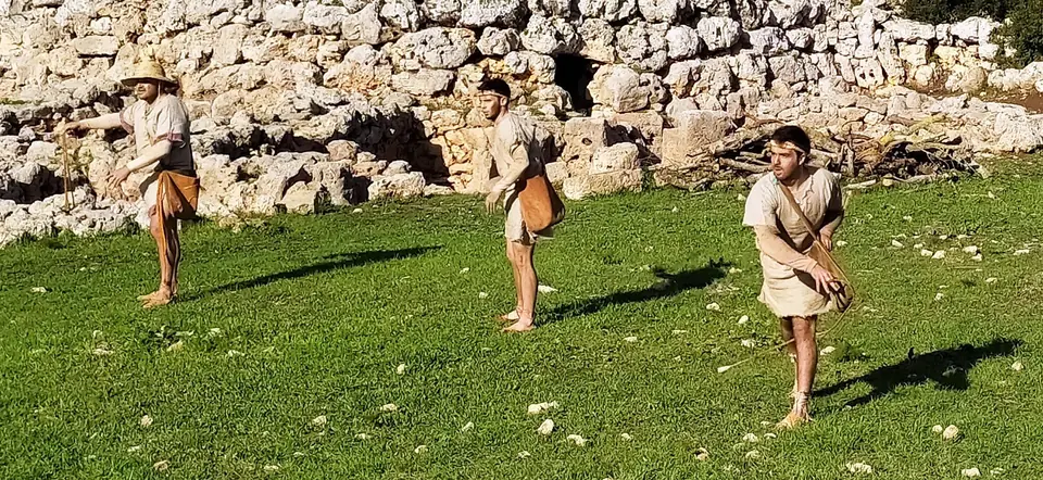 Persones amb vestimenta prehistòrica davant un mur de pedra