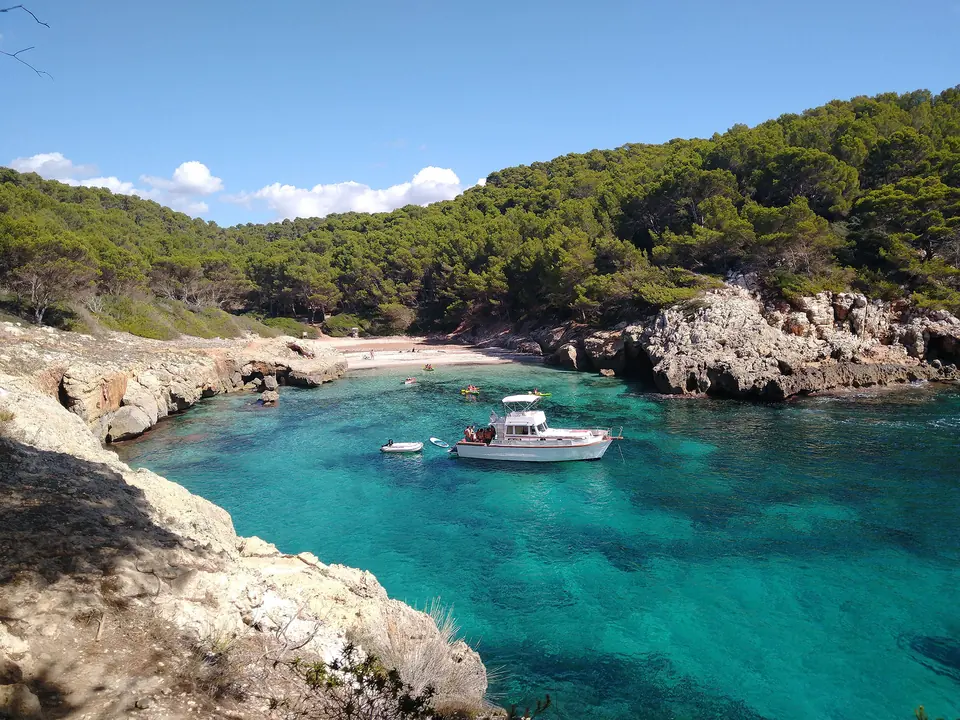 Cala en Fustam: cala d’aigües verdes amb un vaixell entre pins i roques